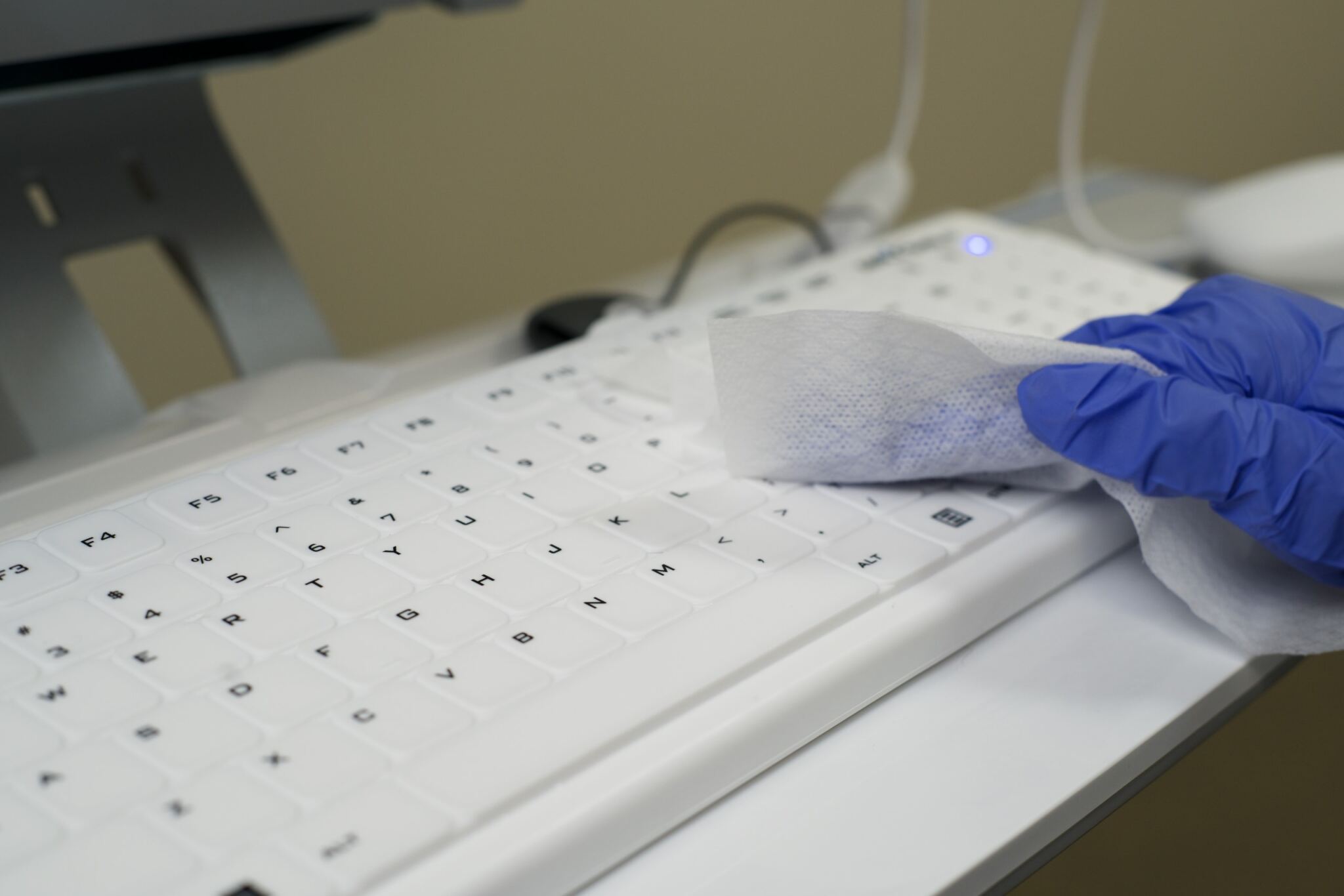 Gloved hands cleaning a white Seal Shield low profile keyboard