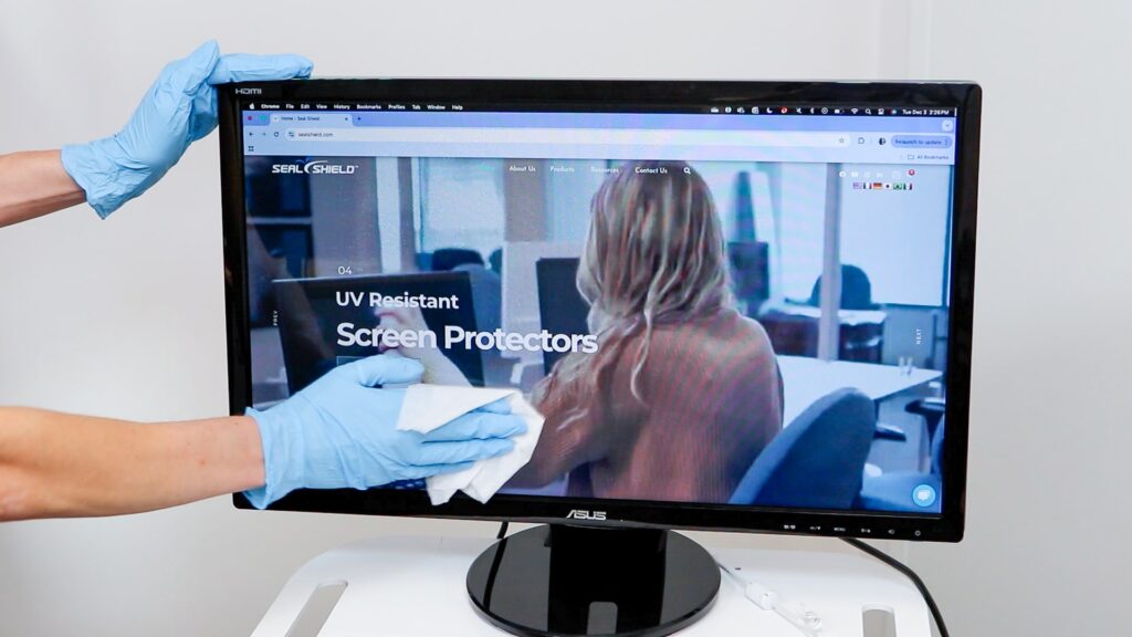 Gloved hand cleaning a Seal Shield Screen Protector on a desktop monitor